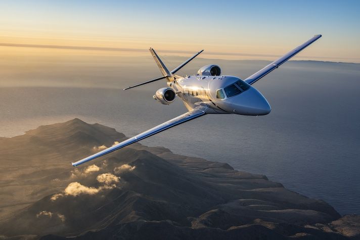 Cessna Citation Ascend achieves FAA certification White private jet with rear-mounted engines flying over coastal island at sunrise with ocean and mountains visible below