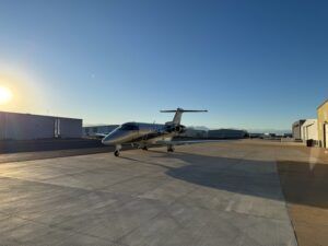 White private jet parked on airport tarmac at sunset with hangars in background