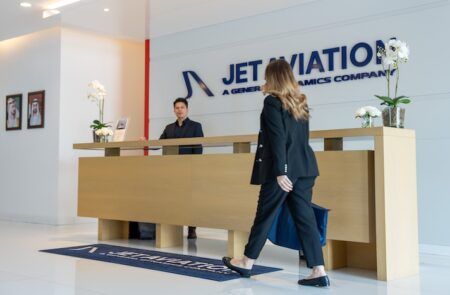 Woman approaching Jet Aviation reception desk with staff member waiting