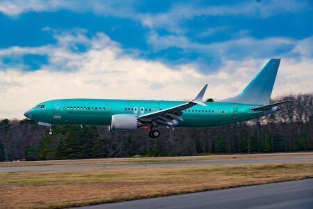 Turquoise Boeing aircraft landing with forest and cloudy sky