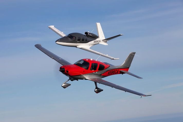 One red aeroplane and one black and white aeroplane in the blue sky