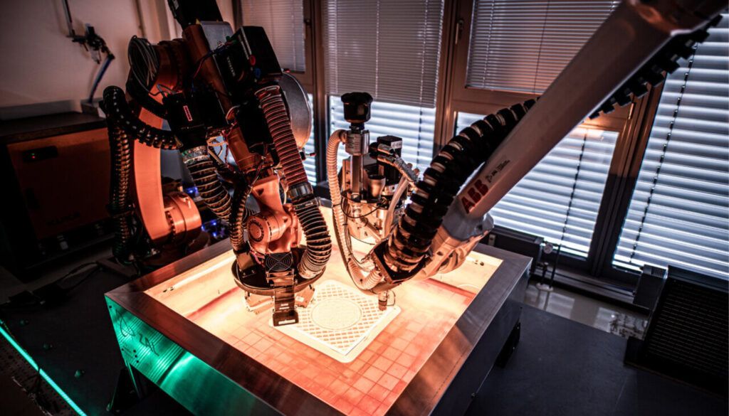 Ramiona robotyczne pracujące nad elementem AM na oświetlonej powierzchni