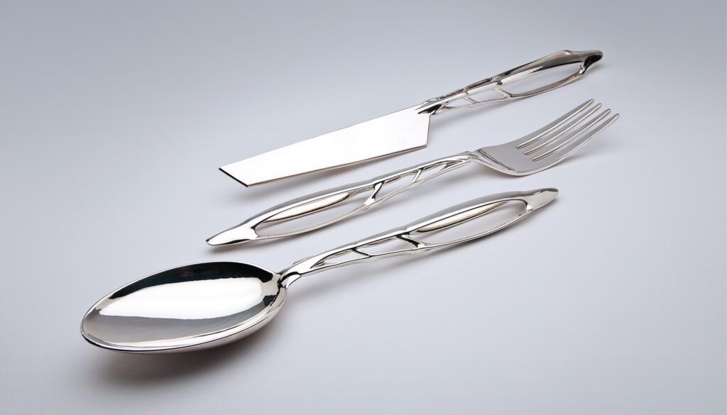 Trzy sztućce z polerowanego srebra z organicznie wyglądającymi otworami w uchwytach