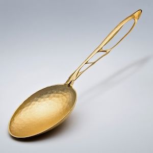 Pojedyncza złota łyżka z organicznie wyglądającymi otworami w rękojeści i efektem młotka