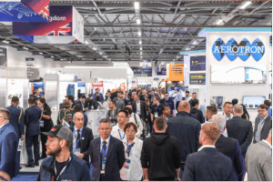 Busy exhibition hall at Farnborough International Airshow showing crowded aisles with international exhibitor stands and visitors in business attire