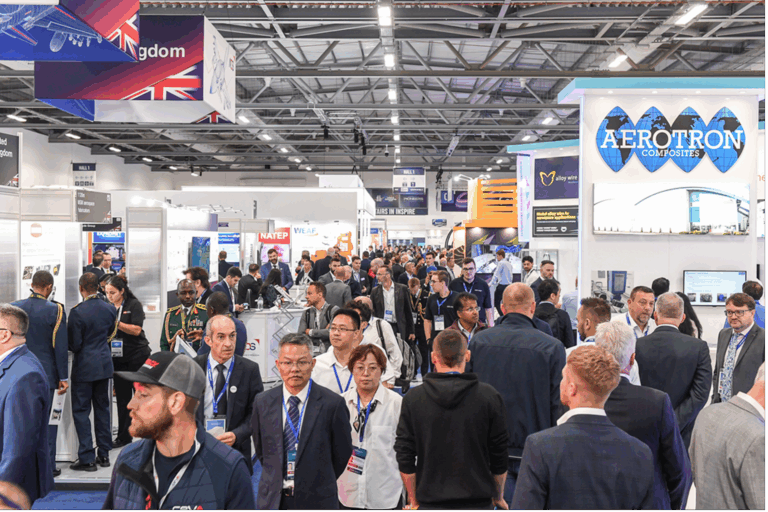 Busy exhibition hall at Farnborough International Airshow showing crowded aisles with international exhibitor stands and visitors in business attire