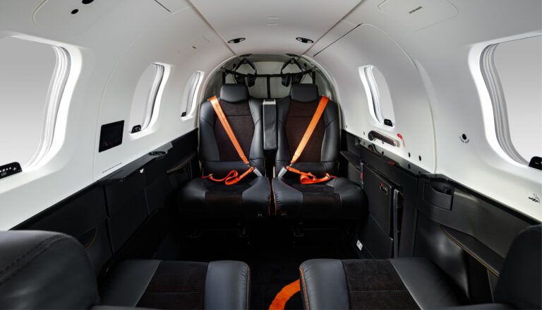 TBM 980 aircraft interior with black seats and orange seatbelts