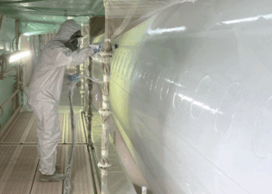 Technician in full protective suit spraying aerospace coating on aircraft fuselage in paint booth