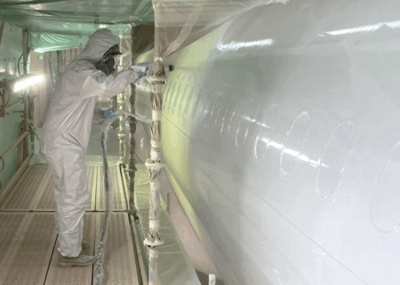 Technician in full protective suit spraying aerospace coating on aircraft fuselage in paint booth