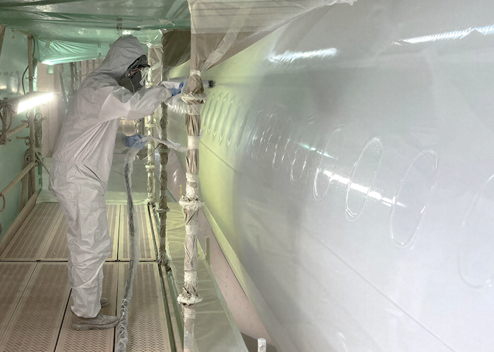 New single-coat AkzoNobel basecoat solution for MROs Technician in full protective suit spraying aerospace coating on aircraft fuselage in paint booth