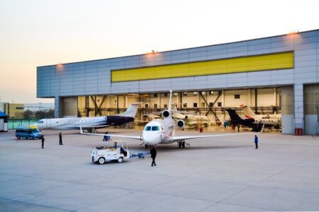 Multiple business jets including a tri-jet aircraft positioned outside and inside ExecuJet Haite’s MRO hangar facility at dusk with ground support equipment visible
