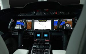 HondaJet Elite II cockpit instrument panel showing three avionics displays with Emergency Autoland active message, dual yoke controls with Honda branding, and centre console