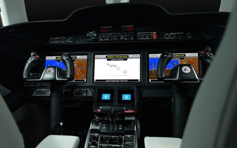 HondaJet Elite II cockpit instrument panel showing three avionics displays with Emergency Autoland active message, dual yoke controls with Honda branding, and centre console