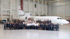 Large group photograph of approximately 100 ExecuJet MRO Services Middle East staff members in business attire and uniforms standing in formation in front of a white private jet inside a modern aircraft hangar.