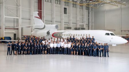 Large group photograph of approximately 100 ExecuJet MRO Services Middle East staff members in business attire and uniforms standing in formation in front of a white private jet inside a modern aircraft hangar.