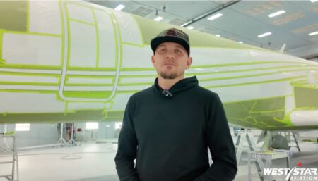 Jeremy Turnbough in front of an aircraft in paint bay with white fuselage covered in green masking lines ahead of stripe painting