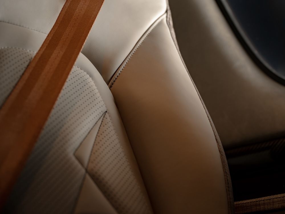 Detail of Cirrus G3 Vision Jet seat upholstery showing cream upholstery with contrasting stitching and tan seat belt