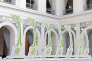 A row of white Crystal Cabin Award trophies with green leaf motifs, displayed in a classical building.