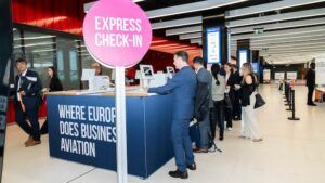 Business aviation professionals queue at an express check-in desk at EBACE, with signage reading “Where Europe Does Business Aviation” on the counter front.