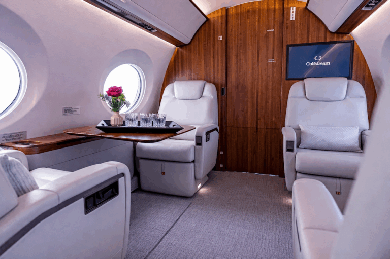 Gulfstream G550 business jet cabin interior with cream leather seats, wood cabinetry, and entertainment display screen mounted on bulkhead