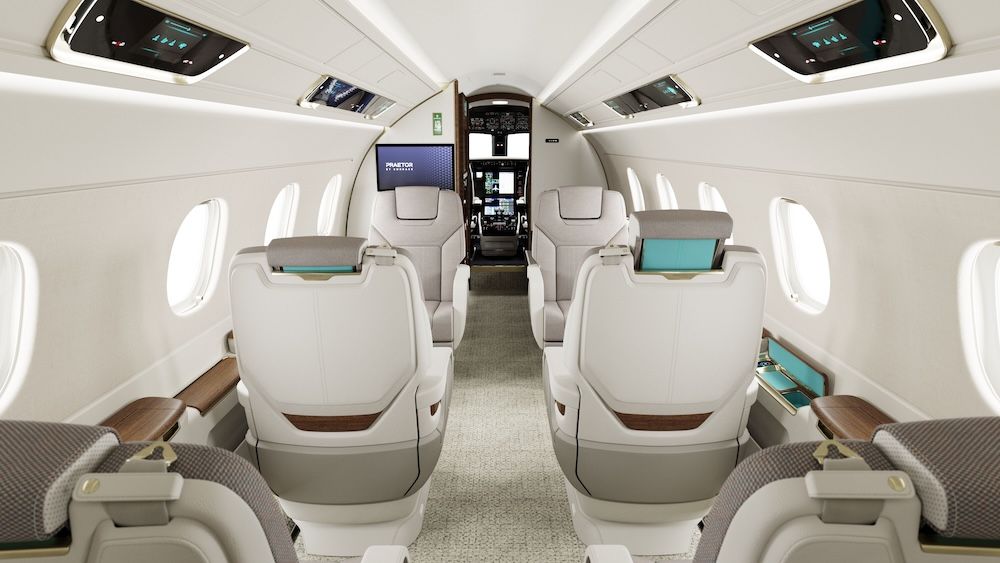 Praetor 500E cabin overview looking forward, showing showing cream leather seats with teal inner headrest panels, bulkhead-mounted display, displays on overhead panels, and central aisle leading to cockpit