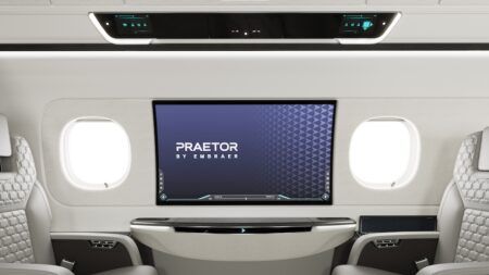 Praetor 600E business jet sidewall with 42in OLED display mounted between two oval windows, showing the Praetor by Embraer logo on screen, and overhead upper tech panel