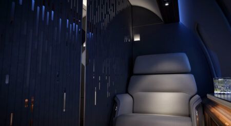 Rendering of a luxurious aircraft interior featuring a deep blue slatted partition wall with subtle integrated lighting, partitioning off a grey leather seat and walnut side table.