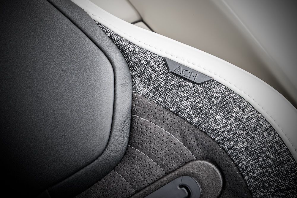Close-up of the seat shoulder bolster in the Airbus ACH140 cabin, showing a combination of perforated dark grey material, grey tweed-style fabric and a small embossed ACH badge on the shoulder section.