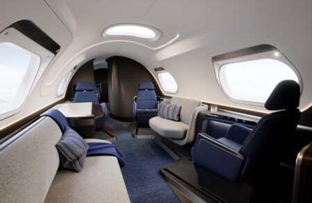 Render of business jet interior concept, showing blue and grey upholstered seats, a divan and large table at side