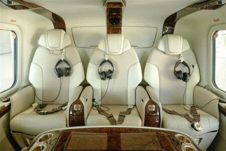 Interior of a Saxon Air AgustaWestland AW139 helicopter showing three cream leather executive seats with headsets, and wood trim console.