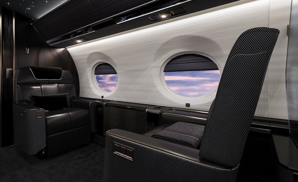 Rendering of a luxury private jet interior featuring black seating with carbon fibre-textured seat backs, a white cabin sidewall with two large oval windows, dark ribbed wall panelling, and subtle overhead lighting.