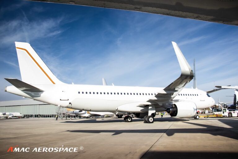 A white ACJ320 with an orange tail stripe at airport