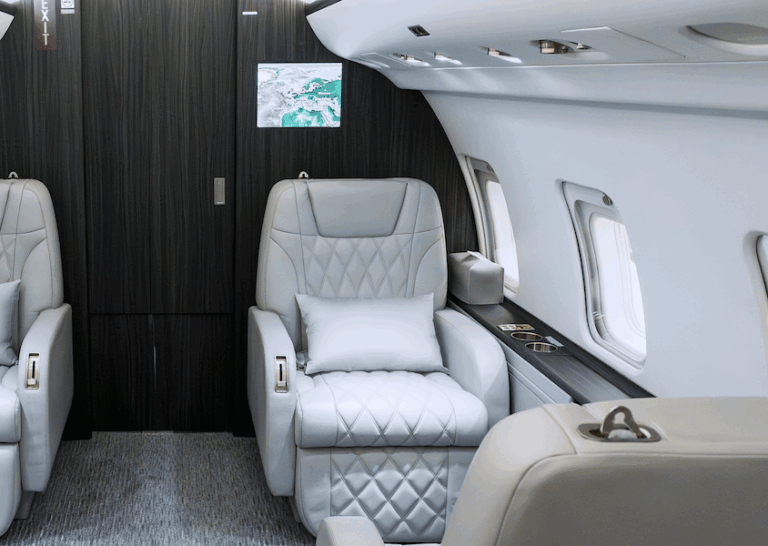 Bombardier Challenger 850 cabin with light leather seats and dark wood veneer on bulkhead with integrated IFE screen