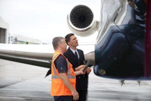 A ground crew member in a high-visibility vest and a pilot in uniform in discussion beside a business jet on airport ramp
