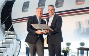 Two men in suits hold a commemorative plaque in front of a Bombardier Global 8000 aircraft