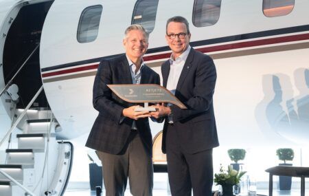Two men in suits hold a commemorative plaque in front of a Bombardier Global 8000 aircraft