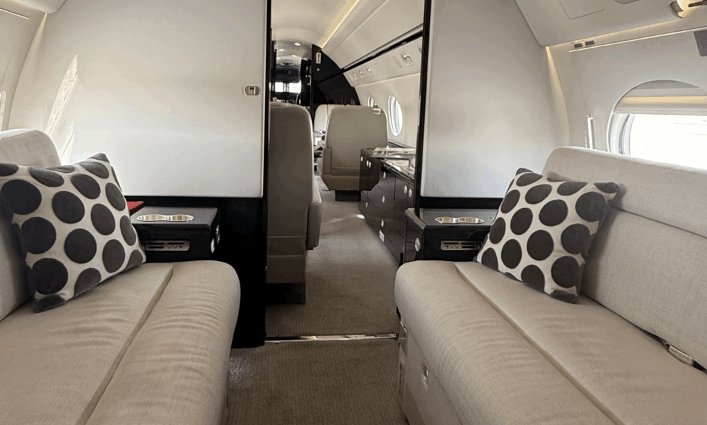 Photograph of the interior of a Gulfstream G550, showing a set dining table with crockery and glassware, lounge seating and a wall-mounted screen.