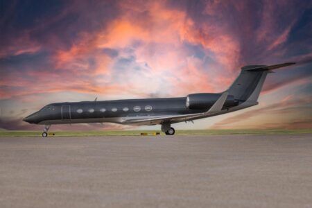 Data automation project flies smoothly for Duncan Aviation A dark-liveried Gulfstream V business jet parked on a tarmac apron, photographed from the port side at ground level against a dramatic sunset sky with pink and orange clouds. The aircraft's swept wings, T-tail and multiple cabin windows are visible along the fuselage