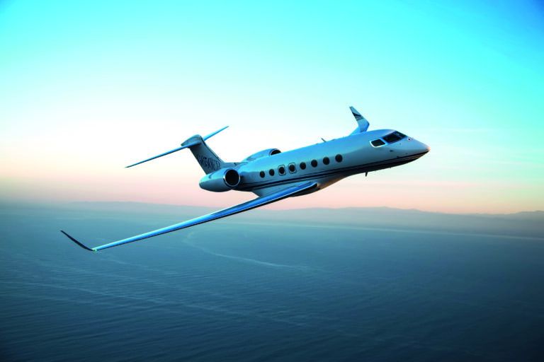 A Gulfstream G650ER business jet in flight over coastal water against a twilight sky
