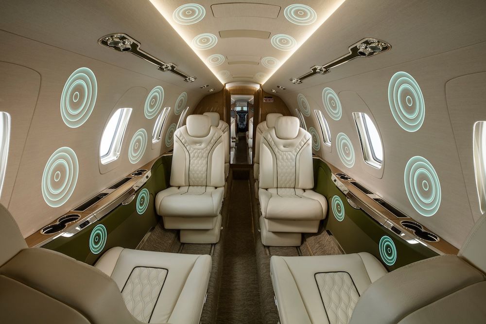 Business jet cabin interior, with teal concentric circle graphics overlaid on the walls and ceiling to illustrate speaker locations throughout the cabin.