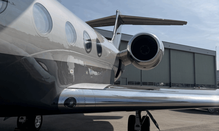 Photograph of the exterior of a Gulfstream G550 business jet on the apron beside a hangar, showing the rear fuselage, wing and engine.