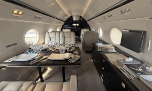 Photograph of the interior of a Gulfstream G550, showing facing sofa-style seats with cushions in a forward cabin section.