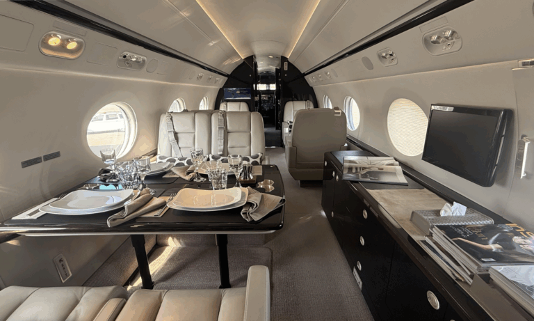 Photograph of the interior of a Gulfstream G550, showing facing sofa-style seats with cushions in a forward cabin section.