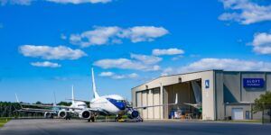 Two aircraft parked outside the Aloft AeroArchitects hangar on a sunny day, with the company name and logo visible on the building.