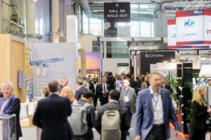 Busy exhibition hall at Aircraft Interiors Expo, Hamburg Messe, showing exhibitor stands including Caynova and Hanse Aerospace with attendees walking the aisles.