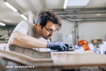 An AMAC Aerospace technician wearing gloves sands a cabin interior panel in a workshop environment.