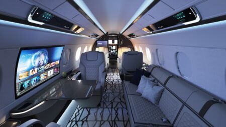 Interior view of the Embraer Praetor 600E cabin showing white leather seating, a large OLED touchscreen Smart Window on the left sidewall, ambient lighting and a divan area.