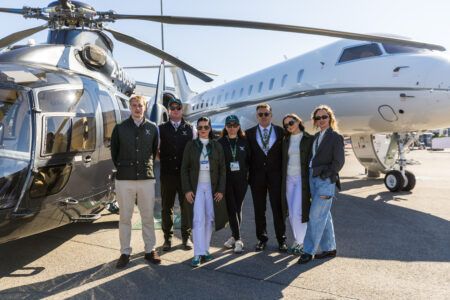 Seven people stand on the static display apron at AERO Friedrichshafen, with an EC155B1 helicopter to the left and a Bombardier Global 5000 to the right
