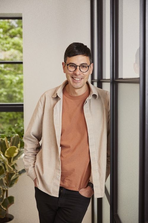 Jérôme Nelet leans against a dark metal-framed glass partition.