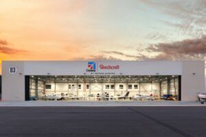 Exterior view of a Textron Aviation service hangar, showing Cessna and Beechcraft branding and multiple aircraft visible inside the open hangar doors at dusk.